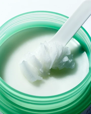 Close-up of a green jar filled with white beauty cream and a white applicator, showcasing the product's texture and consistency.