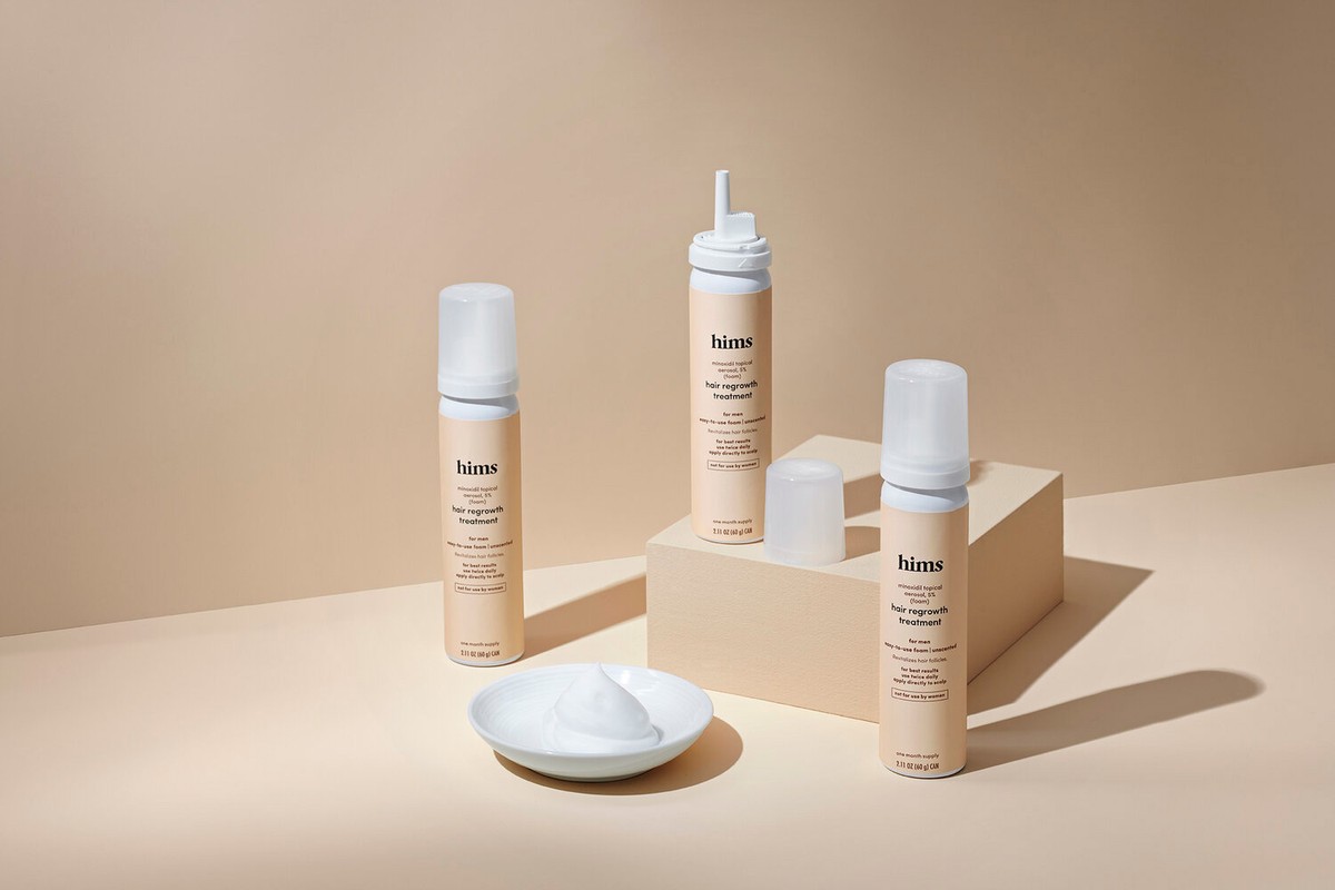 Several bottles of hair regrowth treatment on a beige surface, next to a dish of the white, foamy product from the bottle.