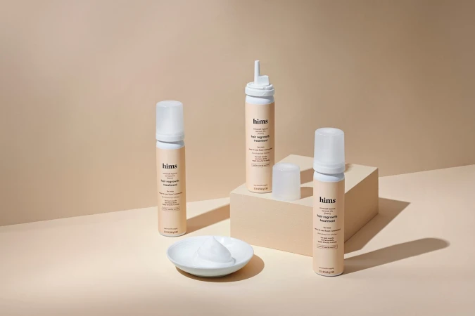 Several bottles of hair regrowth treatment on a beige surface, next to a dish of the white, foamy product from the bottle.