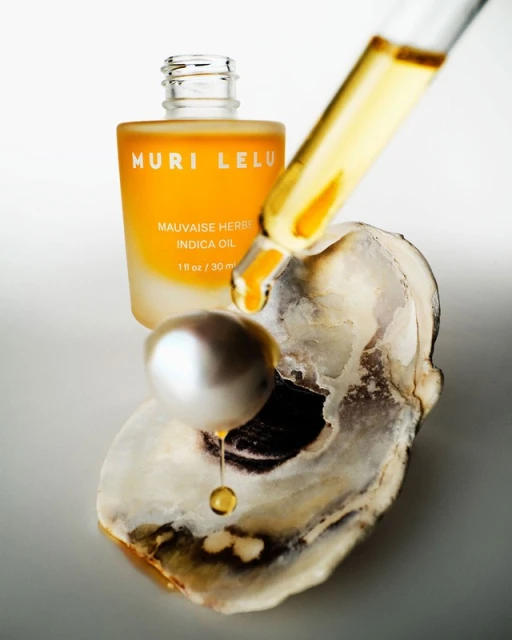 Still life of skincare oil bottle with dropper, pearl, and oyster shell on a neutral background showcasing beauty and skincare.