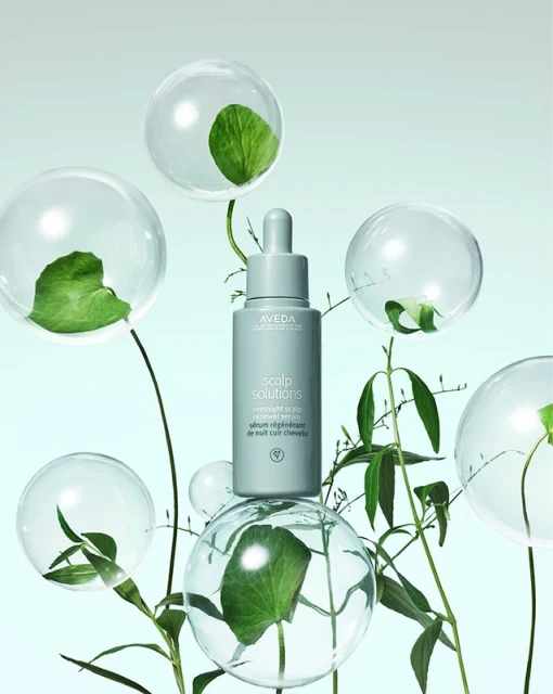 Aveda Scalp Solutions product is centrally placed among transparent bubbles and green foliage against a light blue background. 