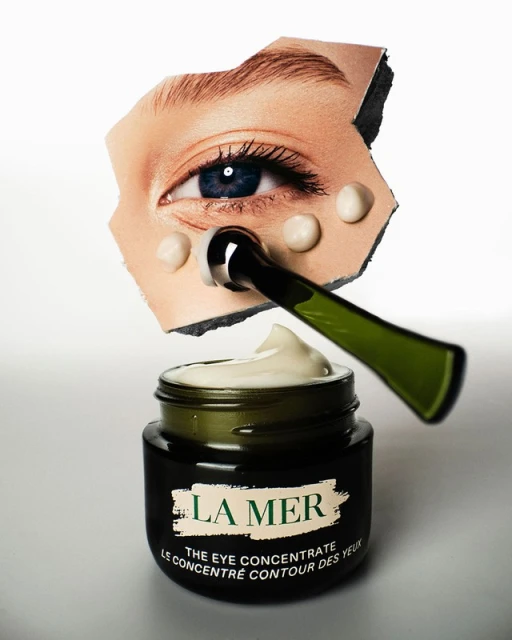 Close-up studio shot of La Mer eye concentrate cream jar, applicator, and eye graphic cutout for beauty and skincare product.