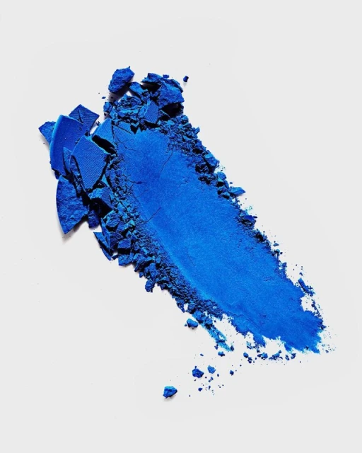 Close-up of vibrant blue eyeshadow powder, showing its texture and pigment against a clean, bright background, beauty product.