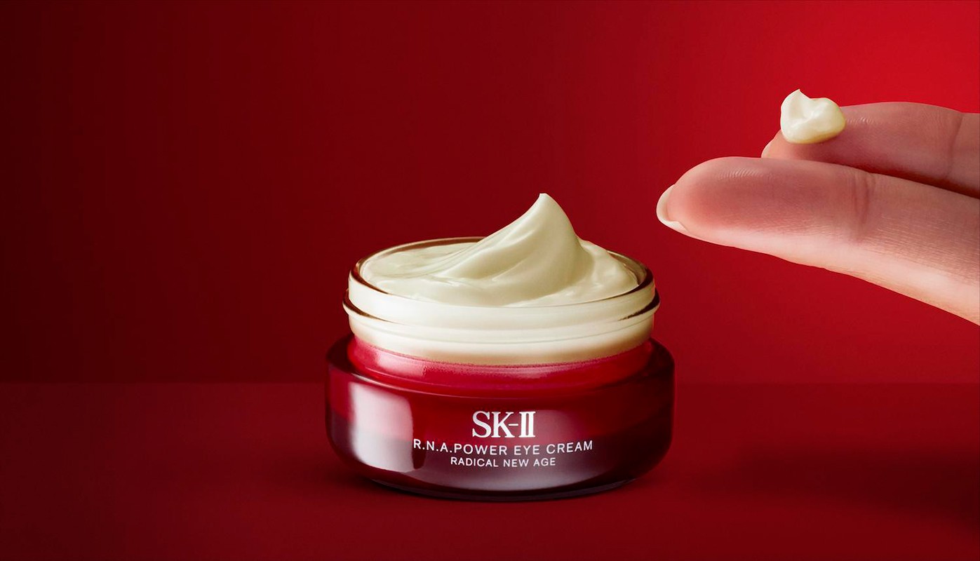 Close-up of SK-II R.N.A. Power Eye Cream jar with finger holding a dollop of cream on a red background. Beauty product shot.