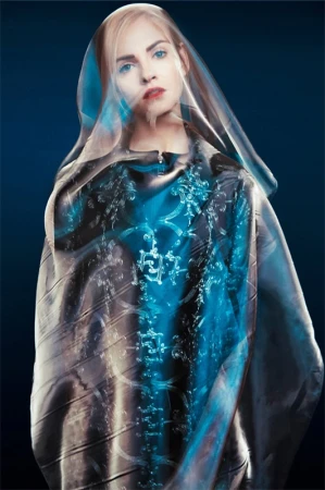 Portrait of a blonde woman wearing a translucent plastic veil over her head and an iridescent blue patterned garment.