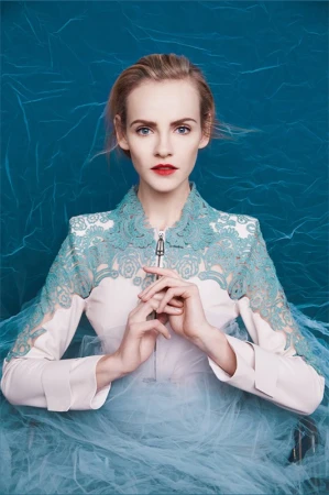 Portrait of a woman wearing a pale pink dress with teal lace collar posing against a textured blue backdrop