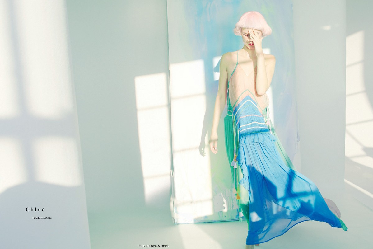 Woman with pink hair wears a long blue ombre dress in a brightly lit studio, fashion editorial.