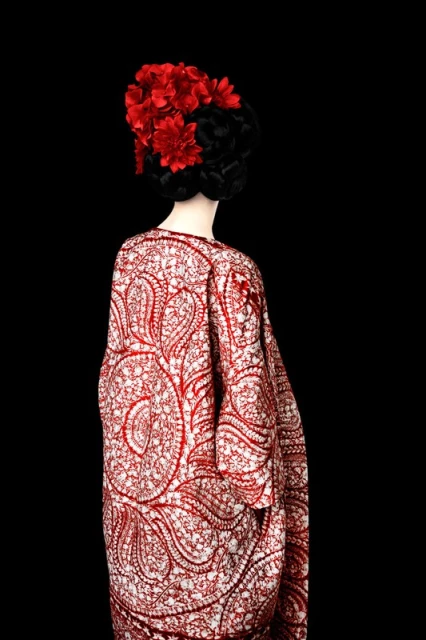 Mannequin wearing a white patterned kimono-style robe with red details and a black and red flower headpiece in a studio setting.