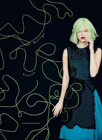 Editorial fashion shot of a model wearing a blue and black dress with a neon green wig against a black background with string art.