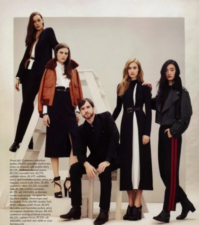 Five fashion models showcase designer apparel indoors; 4 women and 1 man posing. One woman stands on a ladder.