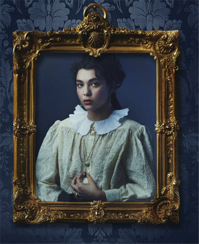 Elegant woman in period-inspired fashion framed against a dark floral wallpaper, radiating vintage charm and classic portraiture style.