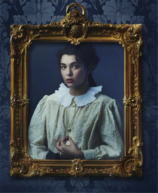 Elegant woman in period-inspired fashion framed against a dark floral wallpaper, radiating vintage charm and classic portraiture style.