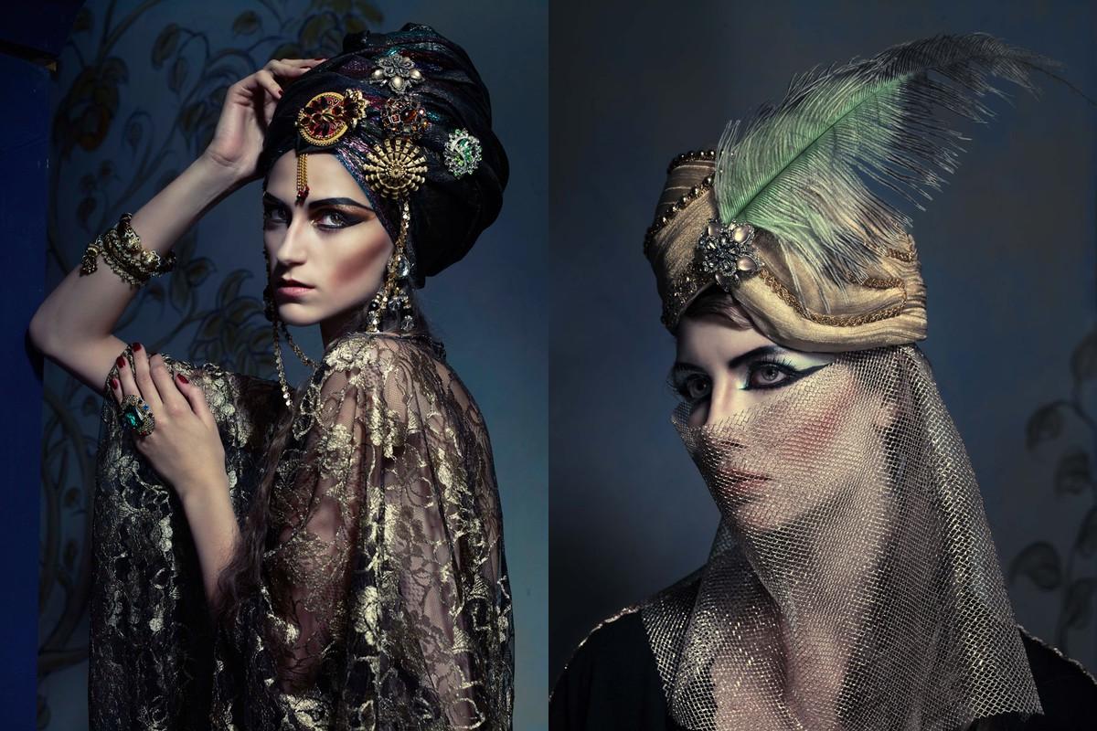Two women in ornate headwear and gold lace. One model in a jeweled turban, the other with a feathered headpiece and mesh veil.