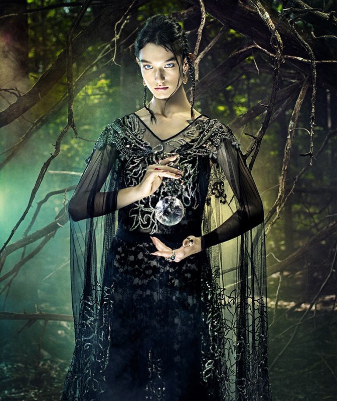 A striking image of a woman in a black dress holding a crystal ball, set against a backdrop of dark, moody woods.