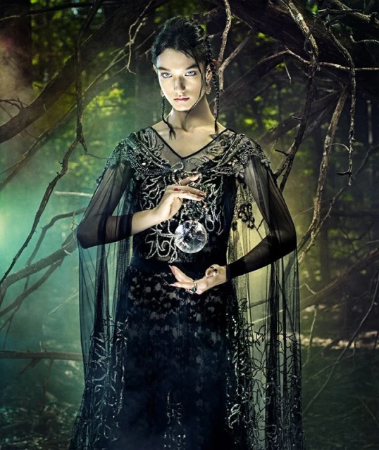 A striking image of a woman in a black dress holding a crystal ball, set against a backdrop of dark, moody woods.