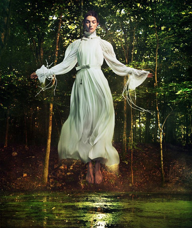 Woman in long flowing white dress levitating in a forest with pond, lit by golden light. Ethereal fashion photo.