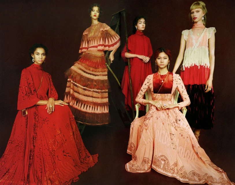 Five diverse fashion models pose in a photo studio wearing long, elegant gowns with intricate details and unique designs against a dark background.