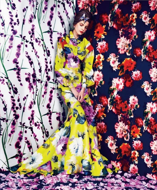 Fashion model wearing a yellow floral gown, poses against floral patterned backdrops of red and purple flowers in a studio setting.
