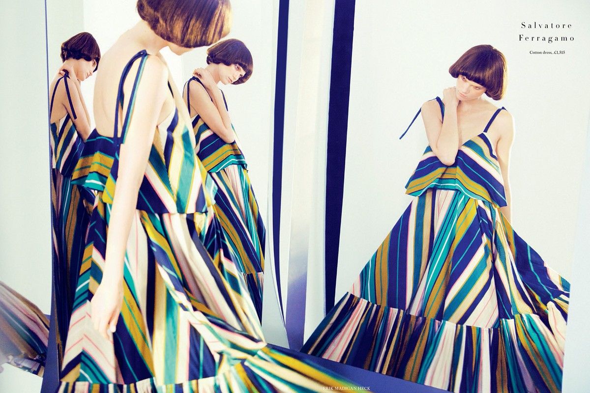Fashion editorial featuring a woman in a flowing, striped Salvatore Ferragamo dress against a white backdrop with black and white vertical stripes.