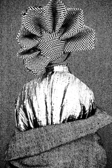 Abstract fashion shot featuring a figure with a textured grey shirt, patterned shawl, and unique headwear, set against a herringbone background.