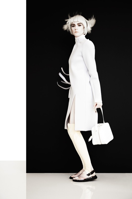 Fashion shot featuring a stylish adult woman in a white coat and accessories, posing against a two-tone black and white backdrop.