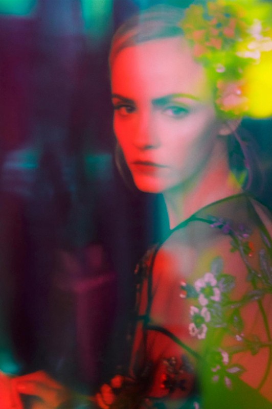 Close-up portrait of a blond woman in a sheer floral top, enhanced by vibrant red, green, and yellow lighting, creating a dreamlike effect.