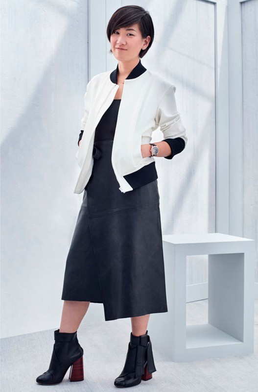 Full-length portrait of a stylish Asian woman in a black dress and white jacket, posing in front of a minimalist white background.