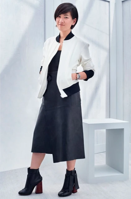 Full-length portrait of a stylish Asian woman in a black dress and white jacket, posing in front of a minimalist white background.