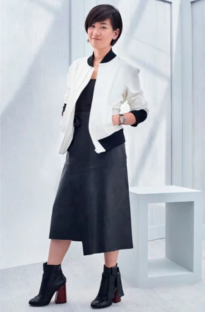 Full-length portrait of a stylish Asian woman in a black dress and white jacket, posing in front of a minimalist white background.