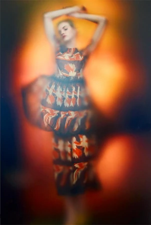 Model in a patterned dress with arms raised against a warm glowing abstract background