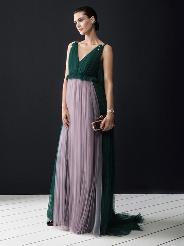 Elegant woman in a green and lilac tulle gown holding a clutch, posing against a dark background in a fashion-style portrait.