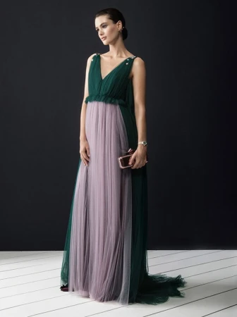 Elegant woman in a green and lilac tulle gown holding a clutch, posing against a dark background in a fashion-style portrait.