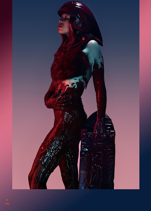 Woman in futuristic costume with headpiece and full body paint leaning on an ornate stone slab in a studio with dramatic lighting.