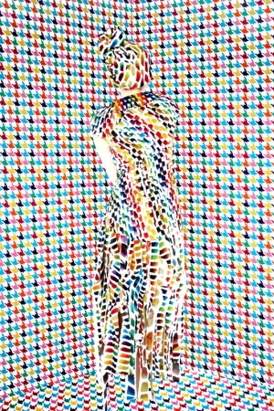 Model standing with back to camera wearing a multi-colored patterned dress and headwrap against a matching houndstooth background
