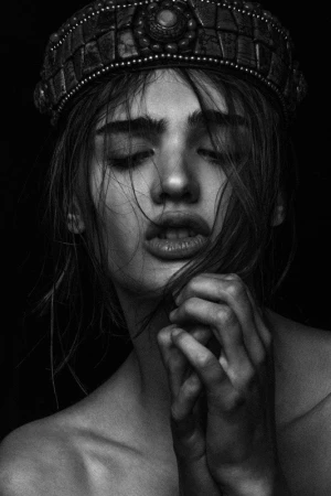 Monochrome portrait of a woman wearing an ornate beaded crown with hands clasped near her face by makeup artist Andriani Vasiliou