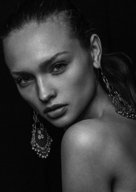 Monochrome portrait of a woman with shoulder pose, featuring ornate earrings and a black backdrop.