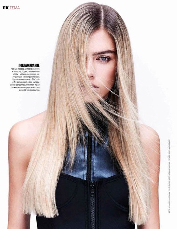 Close-up of a young woman with long blonde hair partially covering her face, wearing a black and blue zip-up top against a white background.
