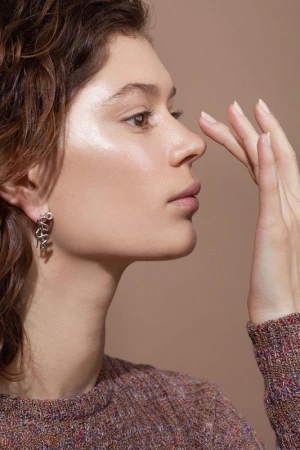 Close-up profile portrait of a woman in profile touching her nose, wearing a textured multi-colored knit sweater and a silver earring.