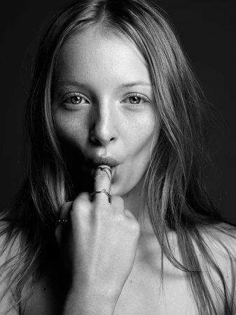 Monochrome close-up portrait of a young woman with rings on her fingers resting near her lips against a dark background