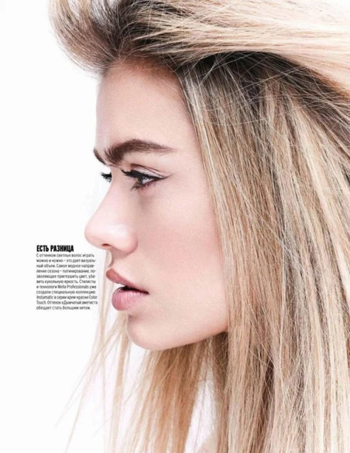Close-up portrait of a fair-skinned young woman with blond hair, dark eyebrows and eyeliner, shot in a photo studio with white background.