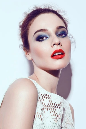 Close-up beauty portrait of a woman with dramatic blue eyeshadow and bold red lipstick wearing a white lace top.
