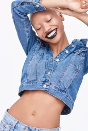 Close-up portrait of a model with short blonde hair and dark lipstick wearing a denim jacket against a white background