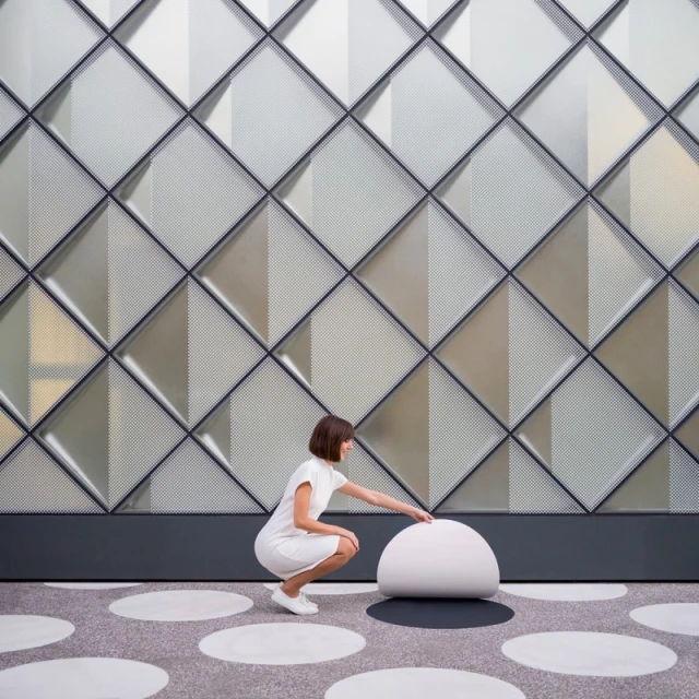 Elegant architectural photo features a woman in white dress interacting with a modern, spherical seat against a patterned wall.