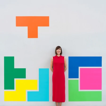 Woman in a red dress standing against a grey wall painted with colorful geometric block shapes in Los Angeles.