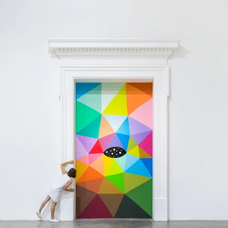 Geometric art on a white door with a woman standing nearby looking at the colorful design of triangles and an oval in the center.