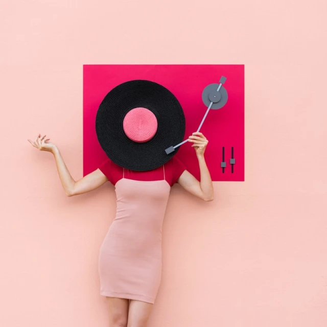 Conceptual fashion shot: female torso in pink dress, arms raised, record player as head against a peach background, pop-art vibe.