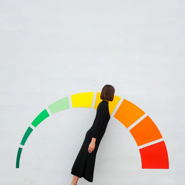 A woman in a black dress stands by a colorful, curved meter graphic, shot in a minimalist studio setting with a flat lay perspective.