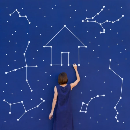 Back view of a woman drawing a house with constellations on a blue wall, creating a whimsical, celestial real estate concept.