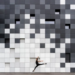 Dancer in black clothing leaping mid-air against a geometric black and white patterned architectural facade in Los Angeles.