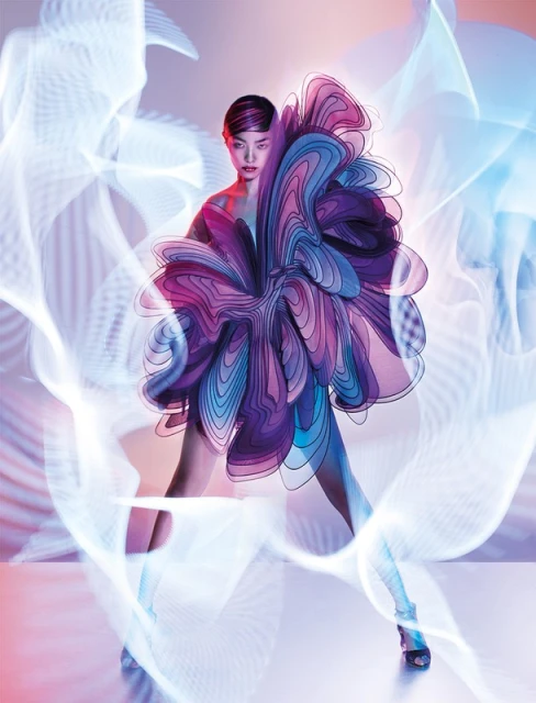 A stylish woman in an elaborate purple dress strikes a dynamic pose against a soft pink backdrop, highlighted by blue and white light effects.